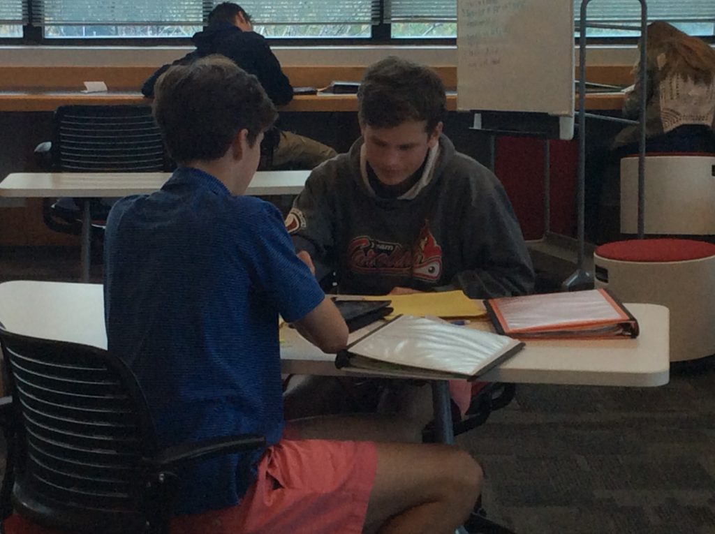 Students help each other in study hall, one working on history and the other on math.